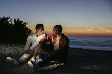 Homosexuelles Paar sitzt in den Bergen über den Wolken bei Sonnenuntergang - LJF00515