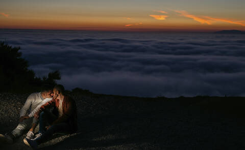 Homosexuelles Paar küssen in den Bergen über den Wolken bei Sonnenuntergang, lizenzfreies Stockfoto
