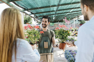 Zufriedene Mitarbeiterin in einem Gartencenter, die den Kunden Pflanzen zeigt - JRFF03448