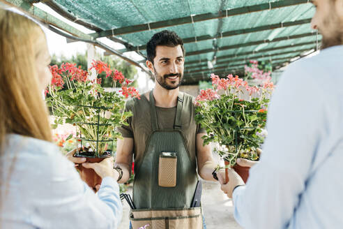 Lächelnde Mitarbeiterin in einem Gartencenter, die den Kunden Pflanzen zeigt - JRFF03449
