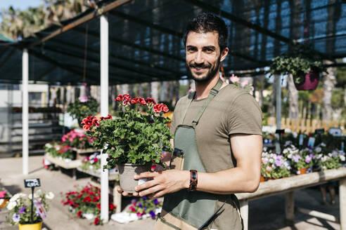Porträt eines lächelnden Gärtners in einem Gartencenter, der eine Blume hält - JRFF03453