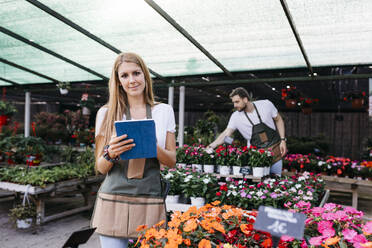 Porträt einer lächelnden Mitarbeiterin in einem Gartencenter, die ein Tablet benutzt - JRFF03505