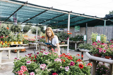 Weibliche Mitarbeiterin in einem Gartencenter mit einem Tablet bei der Pflege von Blumen - JRFF03512