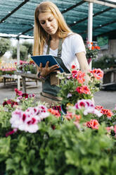 Weibliche Mitarbeiterin in einem Gartencenter mit einem Tablet bei der Pflege von Blumen - JRFF03513