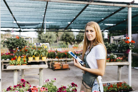 Porträt einer lächelnden Mitarbeiterin in einem Gartencenter, die eine Tafel hält, lizenzfreies Stockfoto