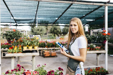 Porträt einer lächelnden Mitarbeiterin in einem Gartencenter, die eine Tafel hält - JRFF03514