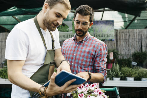 Arbeiter mit Tablet in einem Gartencenter, der Kunden berät - JRFF03517