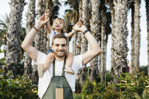 Porträt eines glücklichen Arbeiters eines Gartencenters mit einem Mädchen auf den Schultern, lizenzfreies Stockfoto