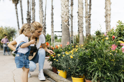 Mitarbeiterin eines Gartencenters zeigt einem kleinen Mädchen Blumen - JRFF03529