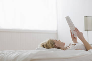 Caucasian woman laying in bed reading paperwork - BLEF12264