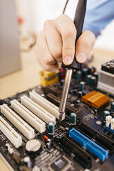 Close-up of technician repairing a desktop computer, soldering a component with tin - JRFF03560