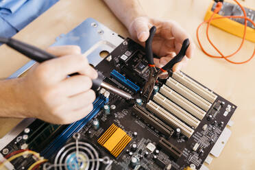 Close-up of technician repairing a desktop computer, soldering a component with tin - JRFF03563