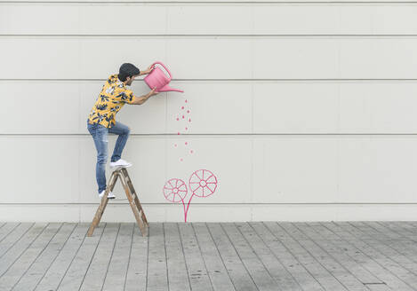 Digitales Komposit eines jungen Mannes, der eine Blume an einer Mauer gießt - UUF18349