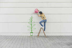 Digital composite of young man watering flower at a wall - UUF18357