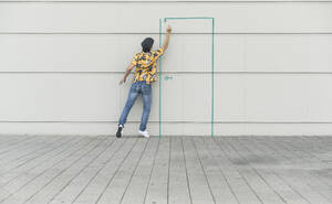Digital composite of young man drawing a door at a wall - UUF18359