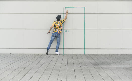 Digitales Kompositum eines jungen Mannes, der eine Tür an eine Wand zeichnet - UUF18359