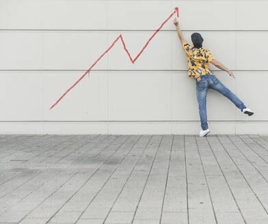 Digital composite of young man drawing a line graph at a wall - UUF18360