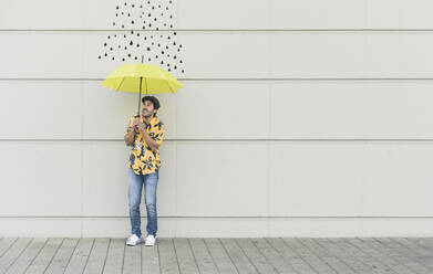 Digitales Komposit eines jungen Mannes, der einen Regenschirm an eine Wand mit Regentropfen hält - UUF18361