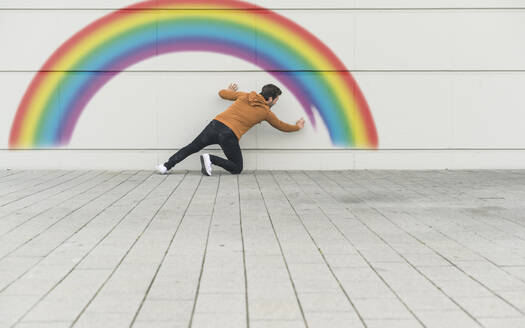 Digitales Komposit eines jungen Mannes, der einen Regenbogen an eine Wand malt - UUF18363