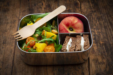 Close-up of healthy salad with sandwiches and fruit in lunch box on table - LVF08219