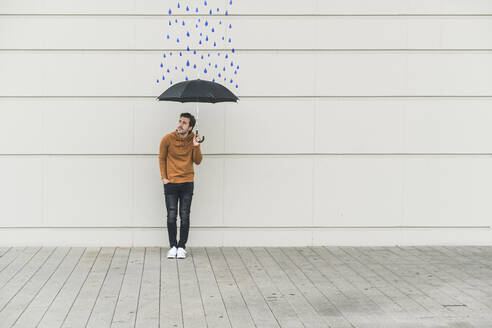 Digitales Komposit eines jungen Mannes, der einen Regenschirm an eine Wand mit Regentropfen hält - UUF18370