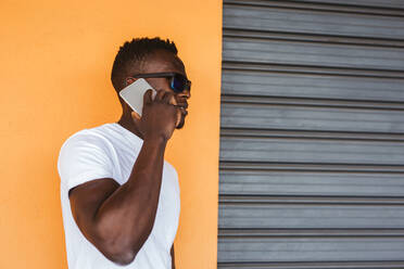 Junger Mann mit weißem T-Shirt und Sonnenbrille spricht mit einem Handy - LJF00536