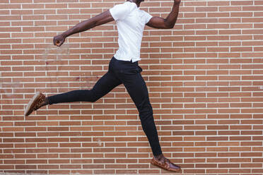 Young man wearing white t-shirt jumping at a brick wall - LJF00538