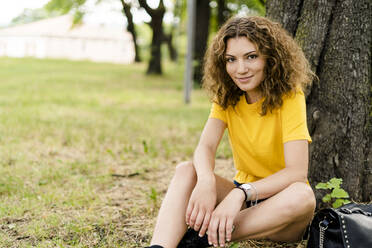 Portrait of smiling young woman sitting in a park - GIOF06991
