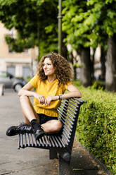 Smiling young woman sitting on a bench - GIOF06993