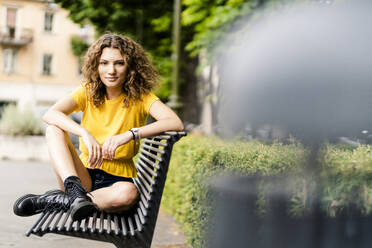 Porträt einer selbstbewussten jungen Frau, die auf einer Bank sitzt - GIOF06994