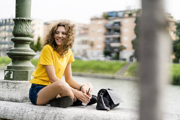 Portrait of happy young woman sitting in the city - GIOF06998