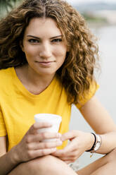 Portrait of smiling young woman holding disposable cup - GIOF06999