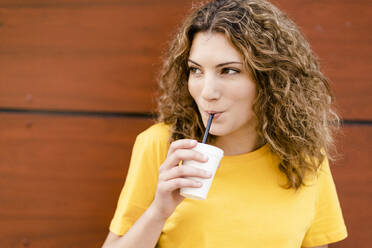 Young woman drinking from disposable cup looking sideways - GIOF07002