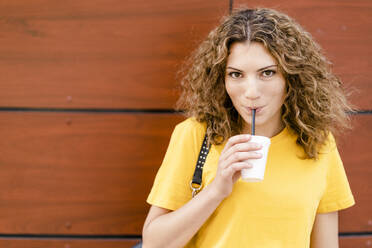 Portrait of young woman drinking from disposable cup - GIOF07003