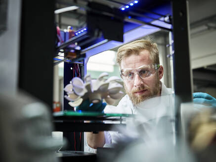 Technician looking at turbine wheel being printed in 3d printer - CVF01403