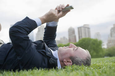 Hispanischer Geschäftsmann, der ein Mobiltelefon in einem Stadtpark benutzt, New York, New York, Vereinigte Staaten - BLEF12350