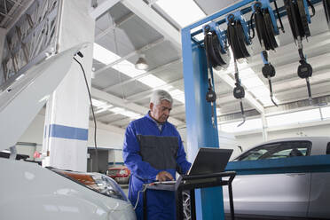 Older Hispanic mechanic using laptop in garage - BLEF12352