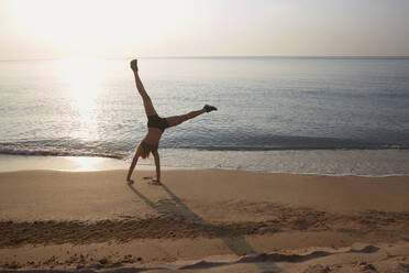 Athlete doing cartwheel on beach - BLEF12353