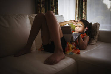 Mixed race girl using digital tablet on sofa - BLEF12384