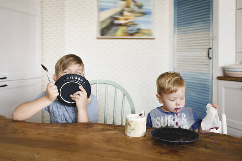 Zwei Brüder mit Tellern, die zu Hause am Tisch sitzen - EYAF00328
