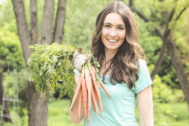 Caucasian woman holding carrots in garden - BLEF12457