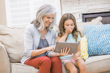 Kaukasische Großmutter und Enkelin benutzen ein digitales Tablet auf dem Sofa - BLEF12548