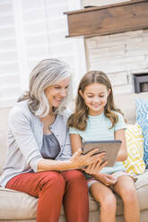 Kaukasische Großmutter und Enkelin benutzen ein digitales Tablet auf dem Sofa - BLEF12549