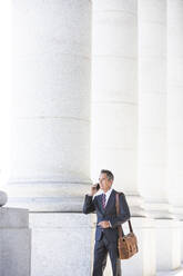 Mixed race businessman talking on cell phone under columns - BLEF12570