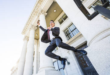 Mixed race businessman jumping for joy outside courthouse - BLEF12592