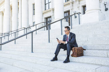 Mixed race businessman using cell phone on courthouse steps - BLEF12600