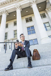 Mixed race businessman using cell phone on courthouse steps - BLEF12601