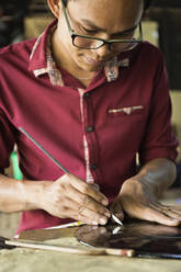 Asiatischer Kunsthandwerker schnitzt traditionelles Design in seiner Werkstatt - BLEF12624