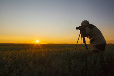 Gemischtrassiger Mann fotografiert ländlichen Sonnenuntergang - BLEF12657