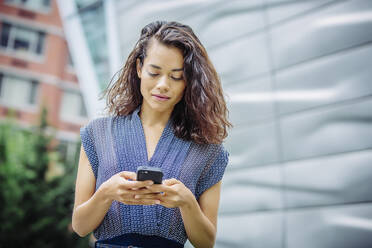 Gemischtrassige Geschäftsfrau, die im Freien ein Mobiltelefon benutzt - BLEF12801